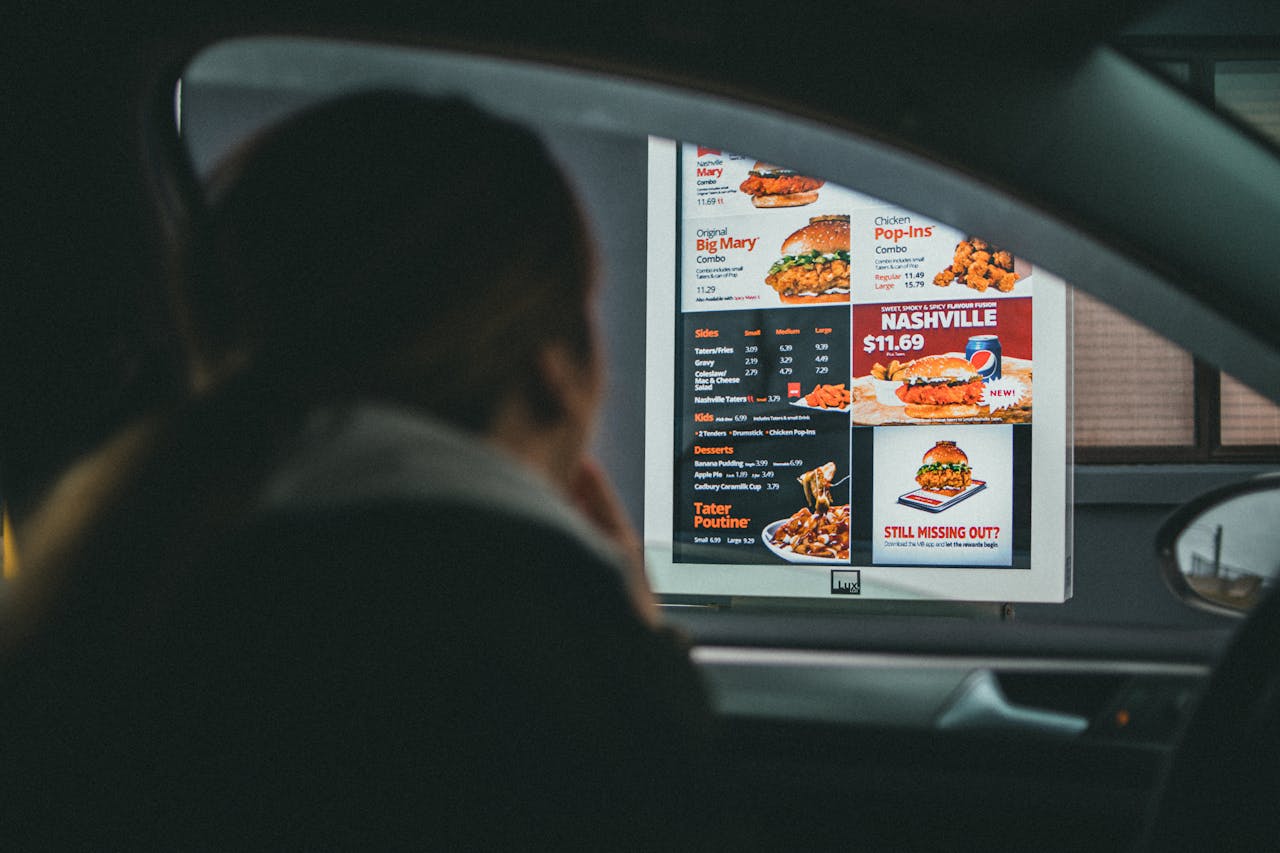 services-02 A woman in a car views the menu at a fast food drive-thru, ready to order her meal.
