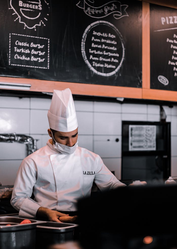 about-01 Chef in traditional attire prepares food in an Istanbul kitchen with menu boards in the background.